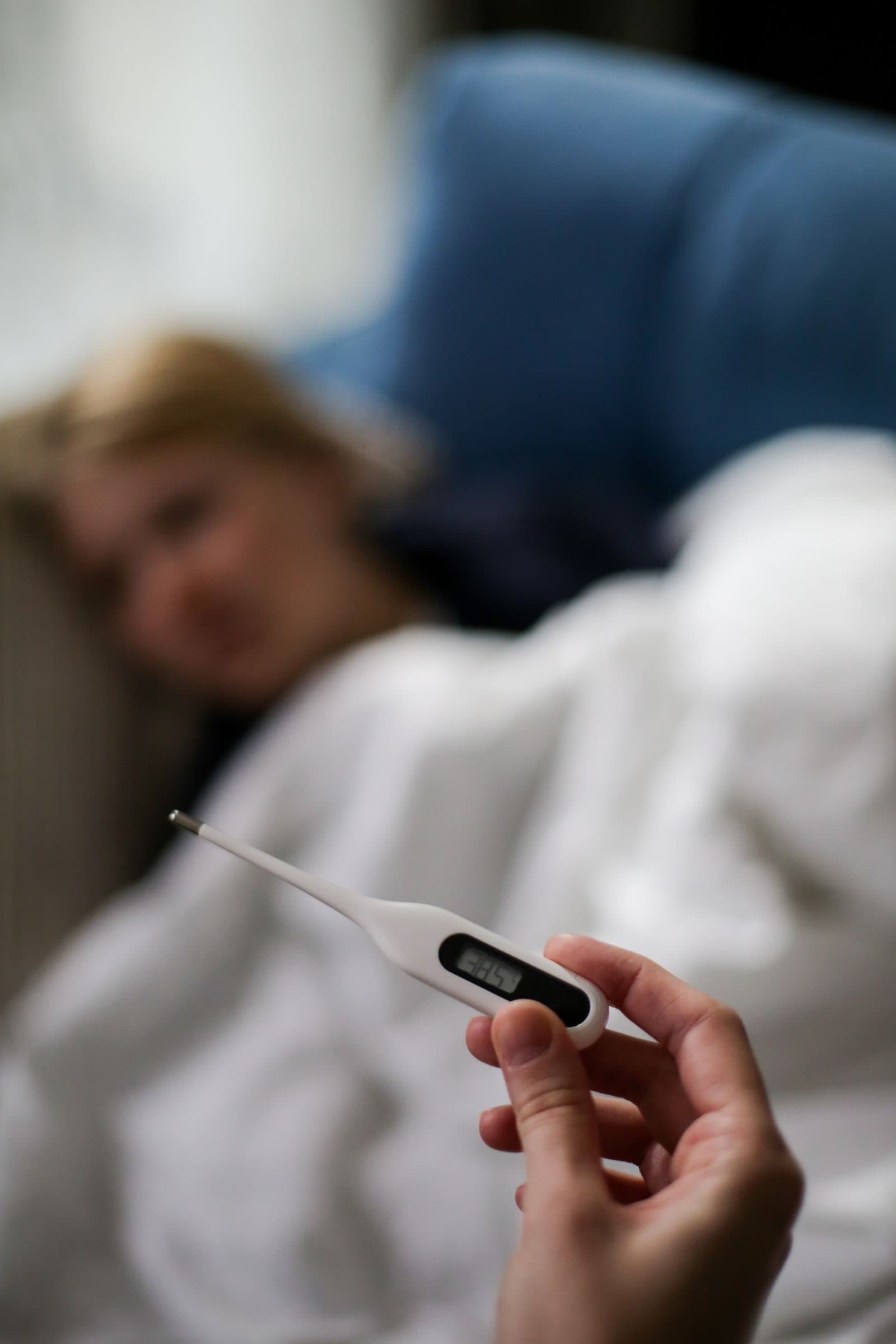 Mão segurando termômetro digital ao lado da cama durante repouso em casa