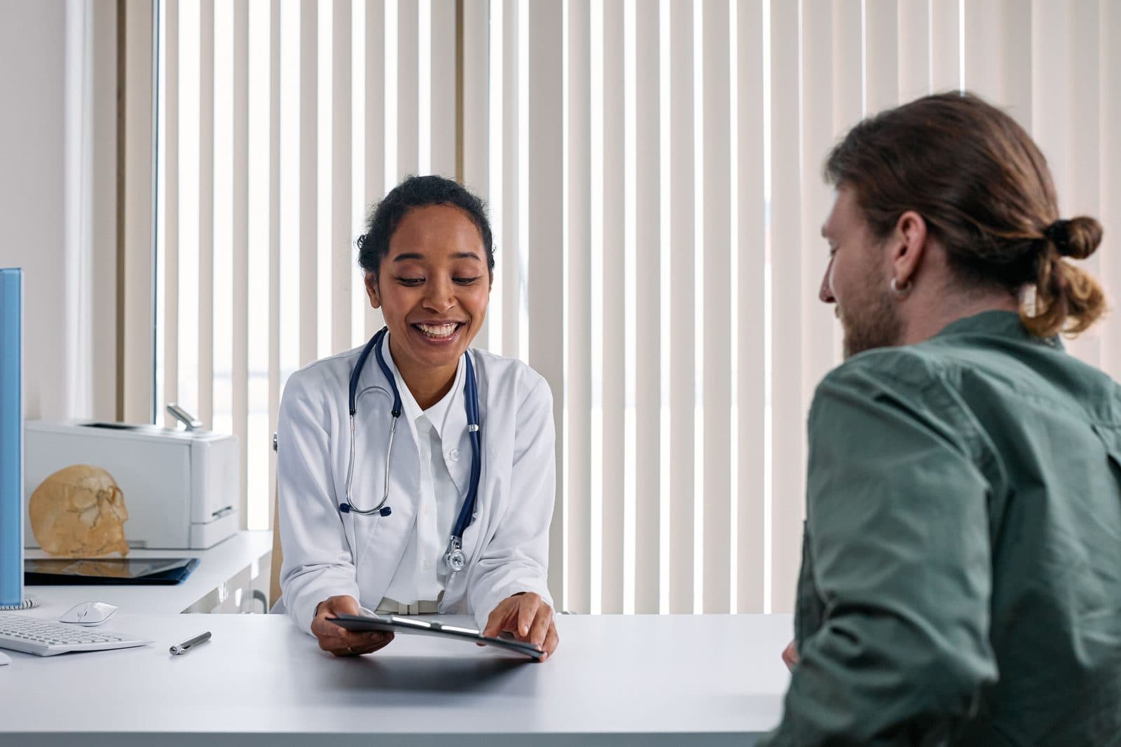 Médica orientando paciente jovem em consultório, com tablet sobre a mesa