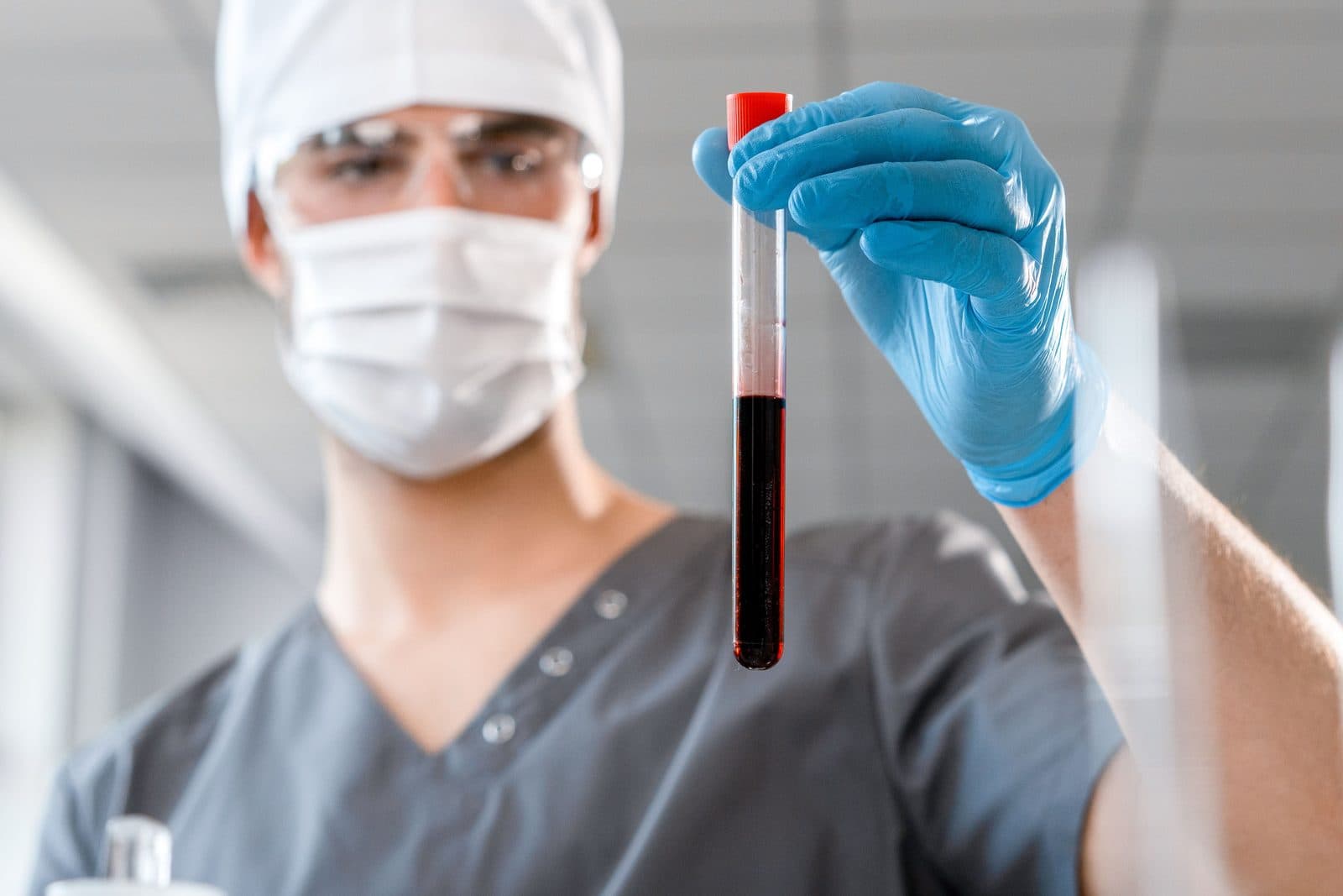 Técnico de laboratório manuseando tubo de coleta de sangue com óculos de proteção